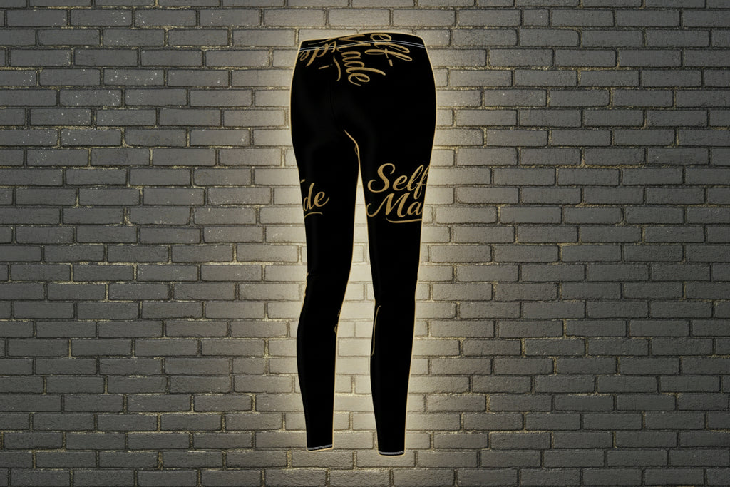 Self Made Gold Script Leggings: Black high-waist women's activewear with motivational print on a gray brick wall.