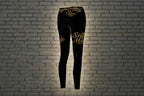 Self Made Gold Script Leggings: Black high-waist women's activewear with motivational print on a gray brick wall.