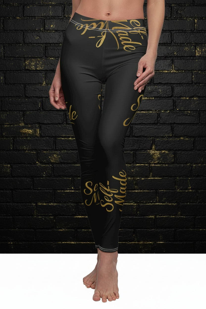 Model wearing Self Made gold script black leggings against a dark brick wall. High-waisted women's activewear.