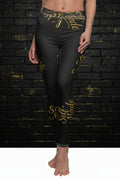Model wearing Self Made gold script black leggings against a dark brick wall. High-waisted women's activewear.