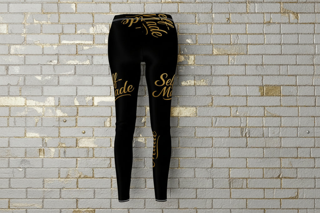 Back view of Self Made gold script black leggings on a grey brick background, showcasing women's compression activewear.