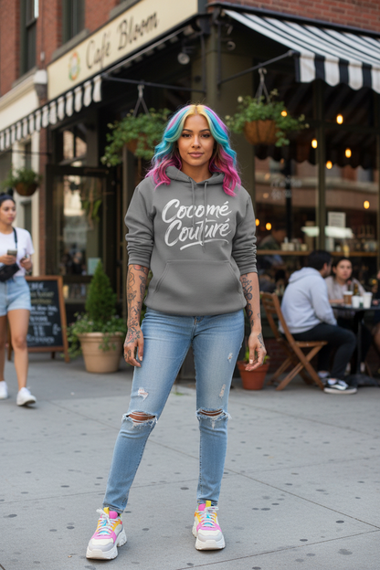 Model wearing CocoMe Couture Unique Look Hoodie in gray with bold white script logo, styled with ripped jeans and colorful hair in urban streetwear setting.