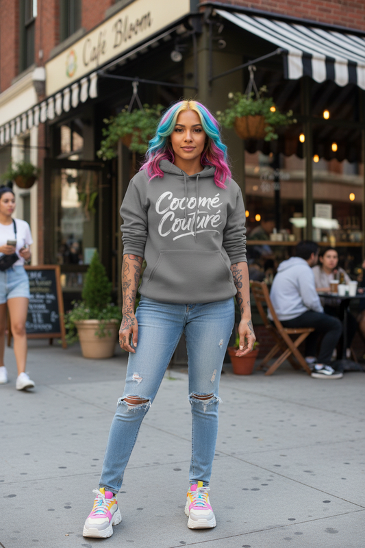 Model wearing CocoMe Couture Unique Look Hoodie in gray with bold white script logo, styled with ripped jeans and colorful hair in urban streetwear setting.