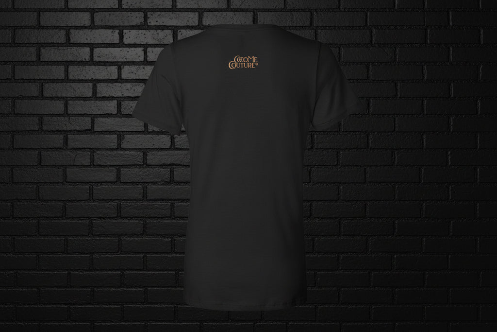 Back view of a black Unbothered Vibe Women's V-Neck Graphic Tee with gold logo on a dark brick background.