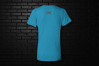 Back view of turquoise Unbothered Vibe women's V-neck graphic tee featuring a small logo against a black brick wall.