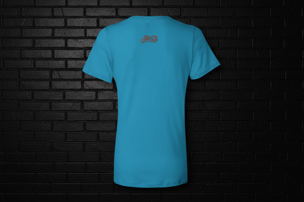 Back view of turquoise Unbothered Vibe women's V-neck graphic tee featuring a small logo against a black brick wall.