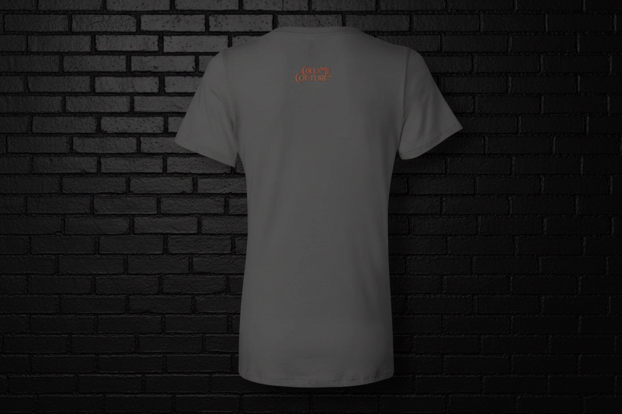 Back view of the grey Unbothered Vibe women's graphic v-neck tee featuring a small orange logo on a dark brick background.