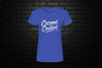 Cocome Couture premium royal blue cotton tee with white script logo on a black brick background.