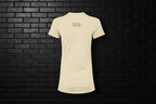 Back view of the Breathe Luxury Slim Fit Tee in cream featuring the Cocome Couture logo on a black brick background.