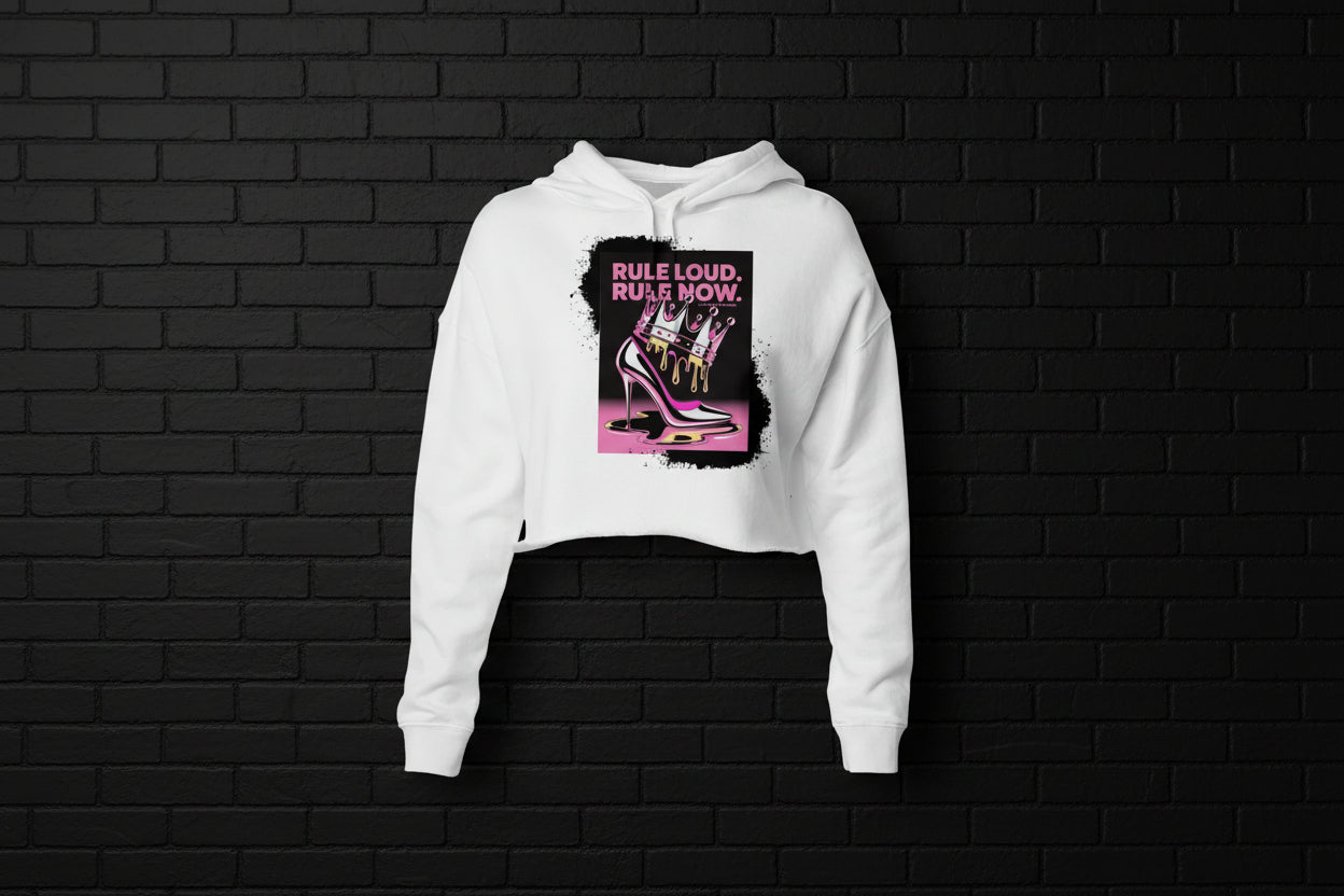 Women's white crop hoodie with Rule Loud crown and stiletto graphic on a black brick background.