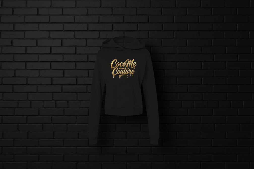 Black CocoMe Couture fleece hoodie with gold dripping logo on a dark brick background — luxe streetwear front view.