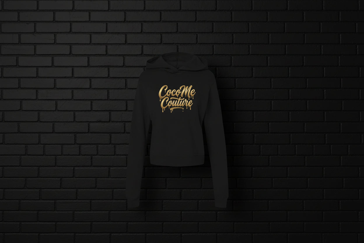 Black CocoMe Couture fleece hoodie with gold dripping logo on a dark brick background — luxe streetwear front view.