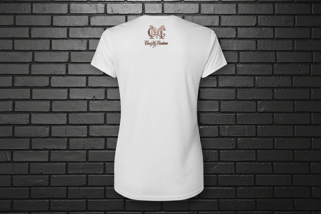 Back view of the Soft but Dangerous Performance Tee in white with Cocome Couture logo on a black brick background.