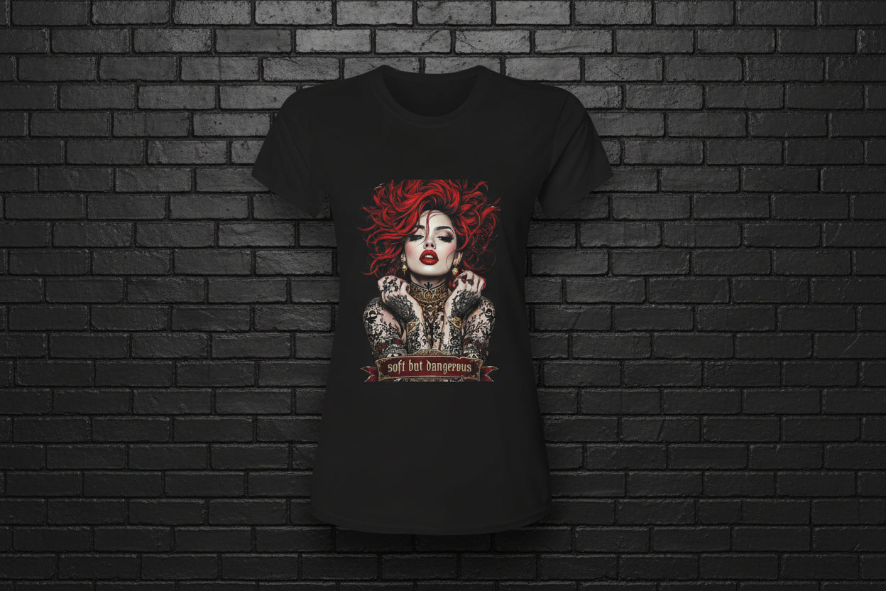 Women's black Soft but Dangerous Performance Tee with red-haired gothic graphic on a brick background.