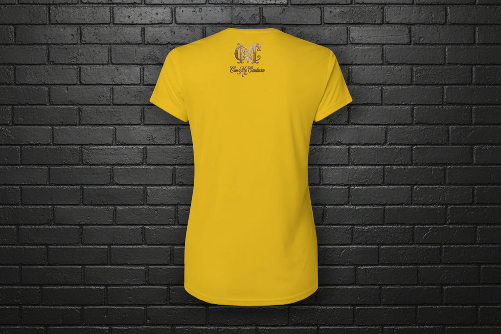 Back view of Soft but Dangerous Women's Activewear Performance Tee in gold with Cocome Couture logo on black brick.