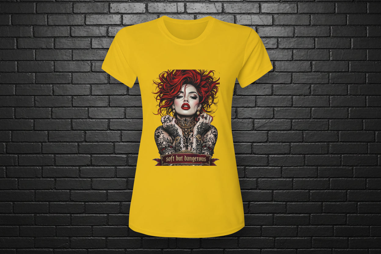 Yellow Soft but Dangerous Performance Tee with red-haired tattooed woman graphic against a black brick wall.
