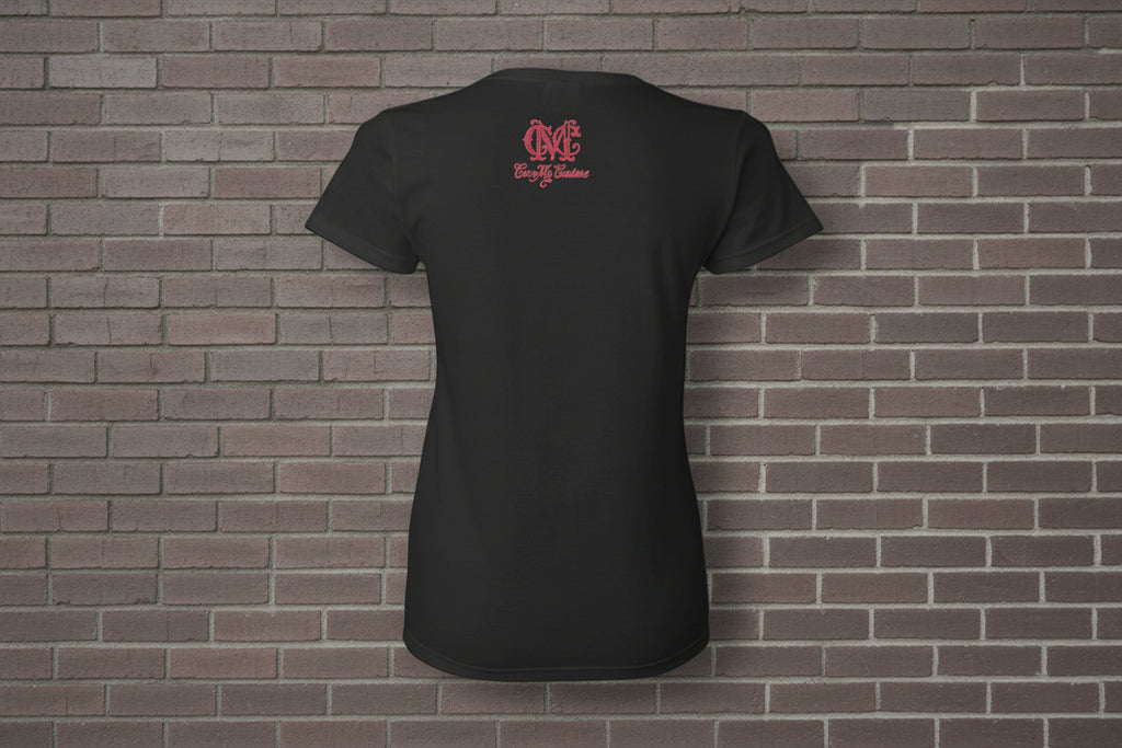 Back view of black cotton women's graphic t-shirt with pink logo on a brick wall background.
