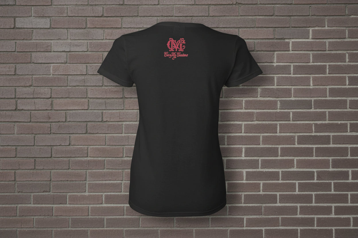 Back view of black cotton women's graphic t-shirt with pink logo on a brick wall background.