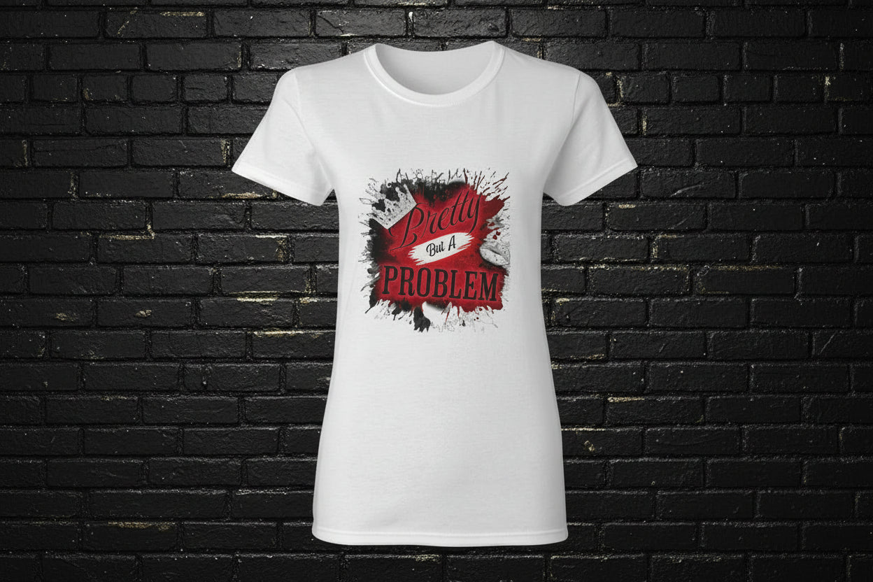 Women's white graphic t-shirt with 'Pretty But A Problem' rebel-luxe print on front against a black brick background.