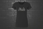 Black heavyweight Aries zodiac shirt with cursive silver text, modern classic fit on a black brick background.