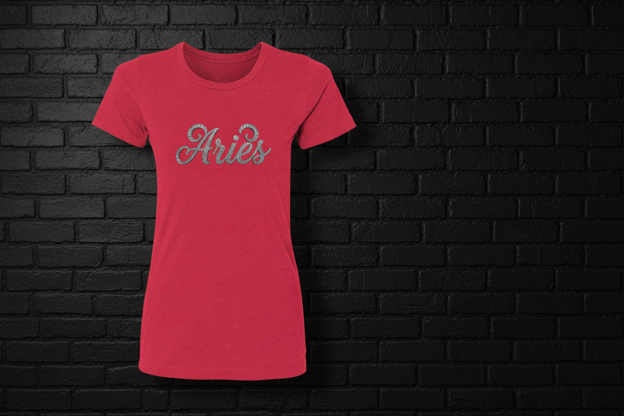 Red heavyweight cotton Aries zodiac t-shirt with silver glitter script design against a black brick wall background.