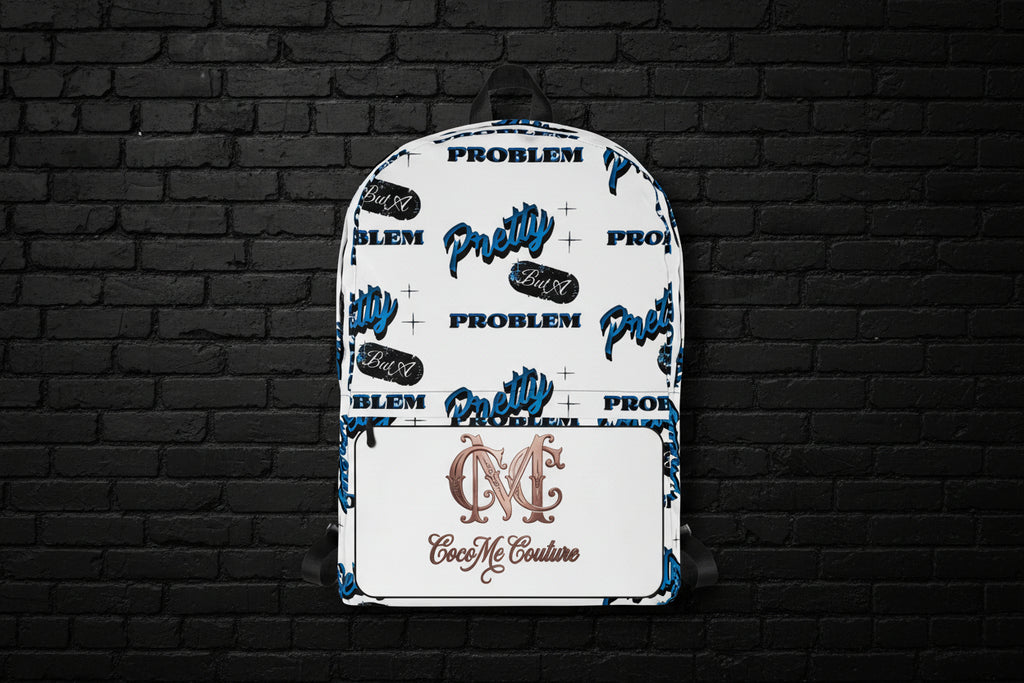 White Pretty But A Problem laptop backpack with blue graphic text and Cocome Couture logo against a black brick wall.