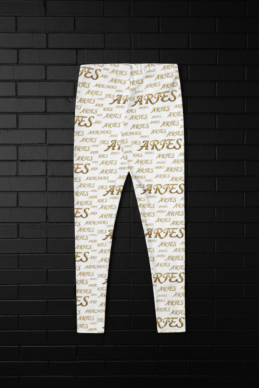 High waisted white yoga leggings with a golden Aries zodiac script all-over print, displayed on a black brick wall.