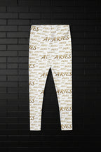 High waisted white yoga leggings with a golden Aries zodiac script all-over print, displayed on a black brick wall.