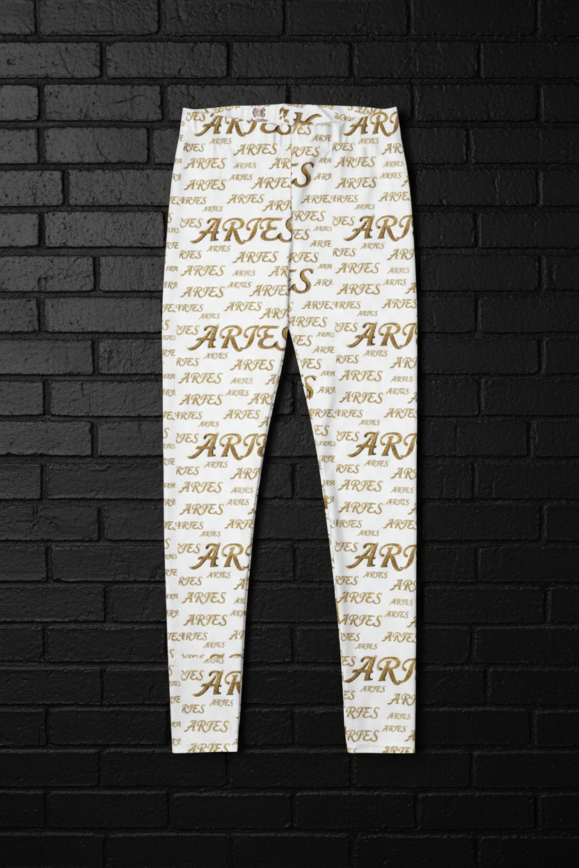 High-waisted white yoga leggings with an all-over gold Aries zodiac print against a dark brick wall background.