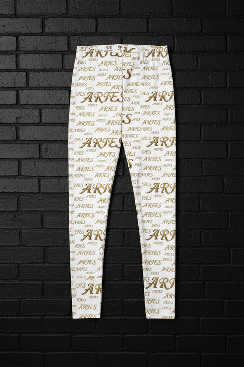 High-waisted white yoga leggings with an all-over gold Aries zodiac print against a dark brick wall background.
