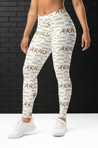 High waisted white yoga leggings with gold Aries zodiac print on model standing against a dark brick background.