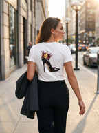 Woman in a white "Royal Rebellion Graphic Tee" with a stiletto and crown graphic, walking outdoors in an urban setting.