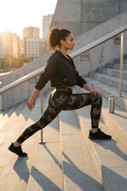 Woman stretching on stairs at sunset, wearing "Self Made Gold Script Leggings — Women's Black Motivational Activewear."